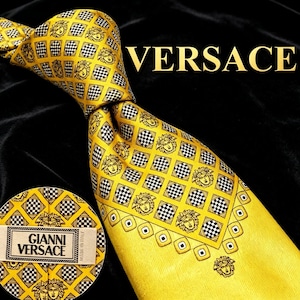 May include: A yellow necktie featuring a repeating diamond grid pattern with alternating black and white checkered squares and Medusa head icons. The tie includes a label reading GIANNI VERSACE MADE IN ITALY and the text VERSACE is visible.