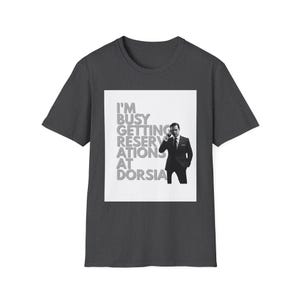 May include: Dark gray t-shirt with a white square graphic. The graphic features the text "I'M BUSY GETTING RESERVATIONS AT DORSIA" and a black and white image of a man in a suit.