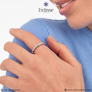 Op de afbeelding: Een zilveren ring met rechthoekige edelstenen wordt op een vinger gedragen. De ring wordt getoond tegen een blauwe achtergrond. Het Eclisse Jewels-logo is linksboven zichtbaar.