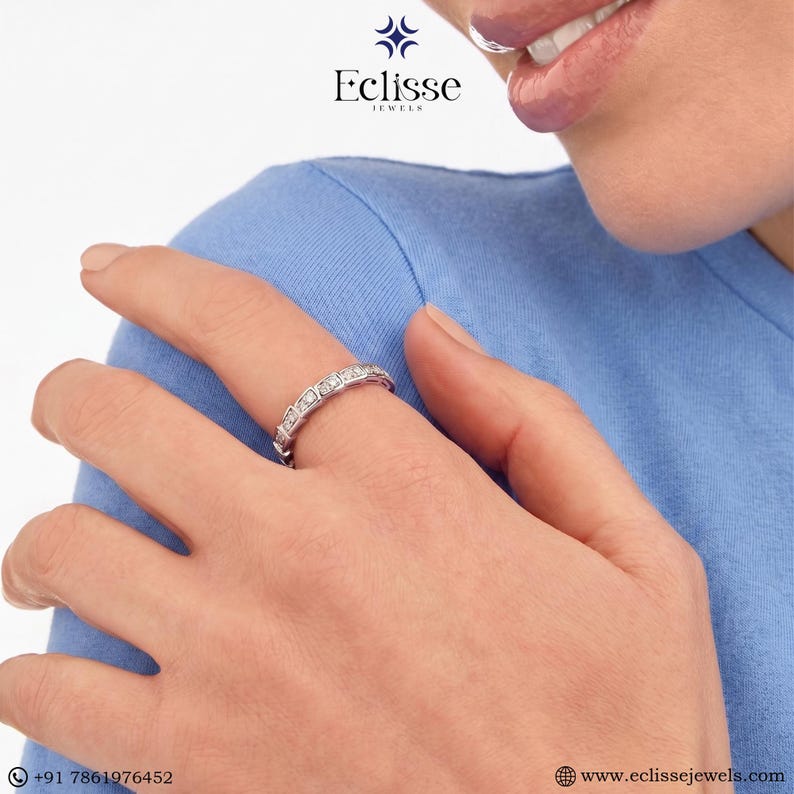 Op de afbeelding: Een zilveren ring met rechthoekige edelstenen wordt op een vinger gedragen. De ring wordt getoond tegen een blauwe achtergrond. Het Eclisse Jewels-logo is linksboven zichtbaar.
