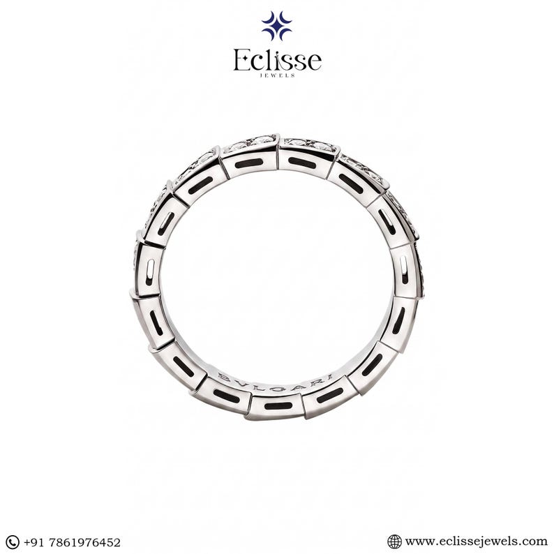 Op de afbeelding: Een zilveren ring met een geometrisch ontwerp, met kleine, sprankelende stenen. De ring is cirkelvormig en heeft het woord "BVLGARI" aan de binnenkant gegraveerd. De ring staat tegen een witte achtergrond.