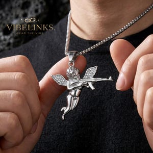 Gold tone Cupid angel pendant necklace in stainless steel with sparkling pavé CZ crystal wings, photographed on a dark background beside a silver tone version, both with 60cm box chains — a bold hip hop jewelry statement piece.