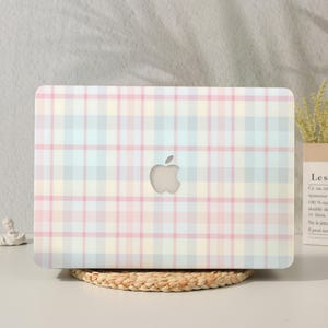 May include: A laptop hard shell case featuring a pastel plaid pattern in soft shades of pink, light blue, and cream. The design includes a central cutout for the Apple logo, showcasing a classic grid-like tartan aesthetic across the entire surface.