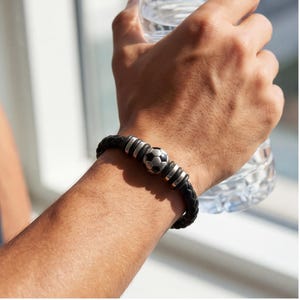 May include: Black braided leather bracelet with a soccer ball charm and silver-tone accents. The bracelet features a central soccer ball design and is secured with a clasp. A stylish accessory for sports enthusiasts.
