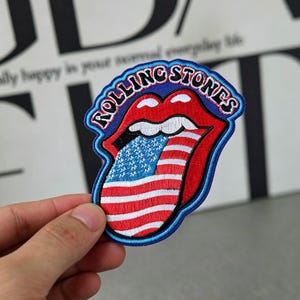 Op de afbeelding: Geborduurde patch met het iconische tong- en lippenlogo van de Rolling Stones. De rode lippen en tong zijn gevuld met het Amerikaanse vlagontwerp, omlijnd in blauw met de woorden "ROLLING STONES" in wit.