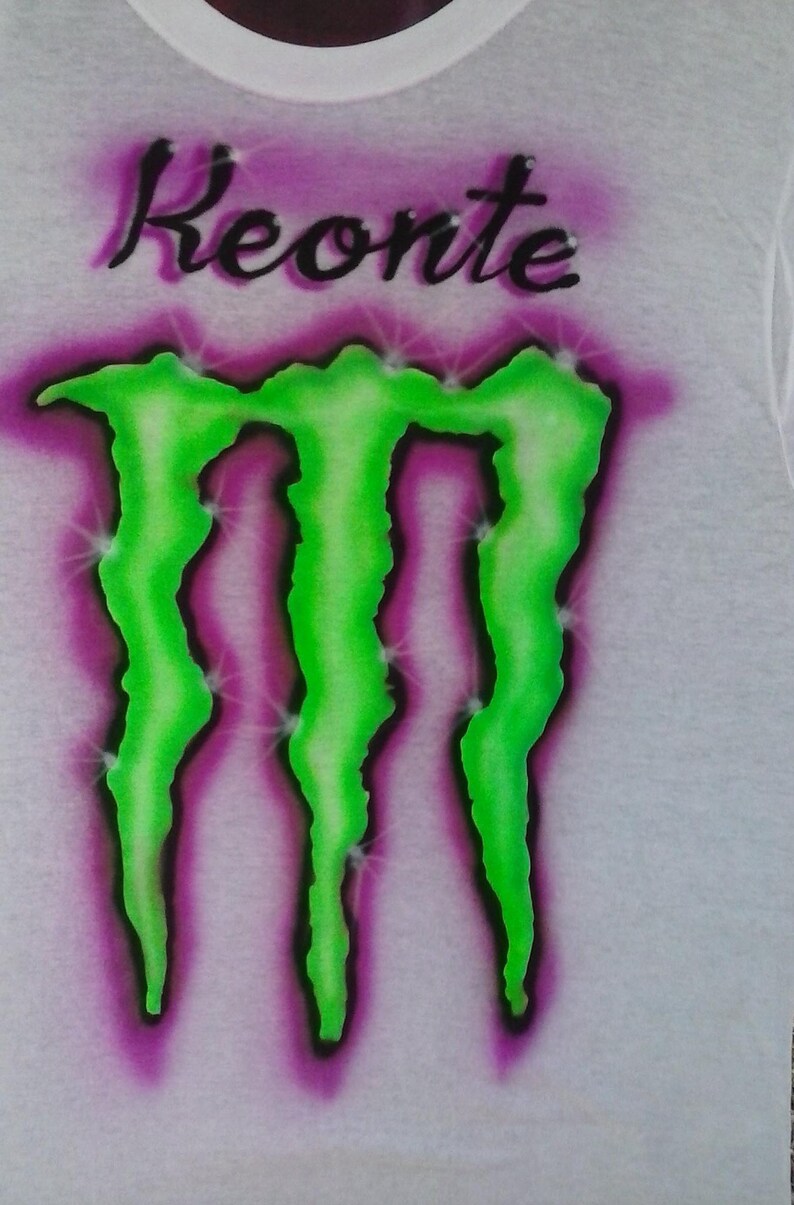 May include: White t-shirt with the name "Keonte" in black script above a neon green and purple graphic. The graphic is a stylized three-claw design with a purple and white gradient background.