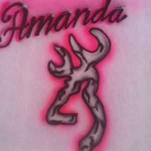 May include: Pink and white airbrushed design featuring the name "Amanda" in cursive script above a gray and black stylized emblem. The emblem has a pink outline.