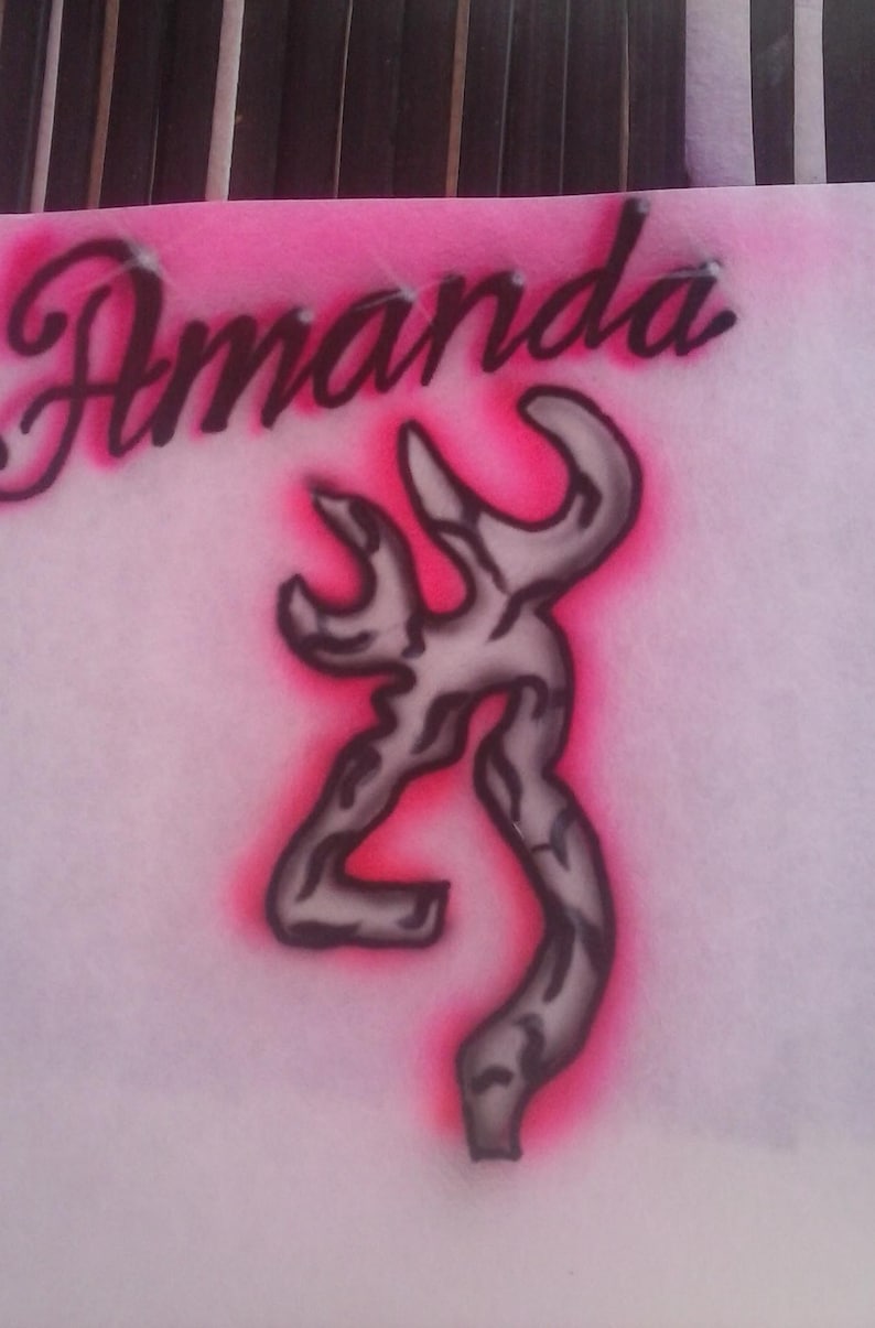 May include: Pink and white airbrushed design featuring the name "Amanda" in cursive script above a gray and black stylized emblem. The emblem has a pink outline.