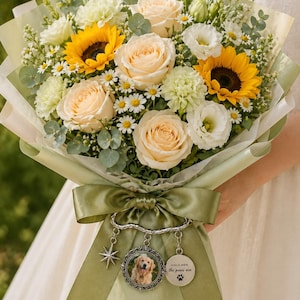 May include: A vibrant bouquet featuring sunflowers, peach roses, white daisies, and greenery, wrapped in light green paper and tied with a green satin ribbon. Charms with a star, a dog photo, and the text "Home is where the paws are" are attached.