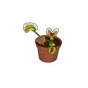Puede incluir: Una pegatina con una caricatura de una Venus atrapamoscas en una maceta marrón. La planta tiene hojas verdes y rojas, y un pequeño letrero que dice "FEED ME!". La pegatina está sobre un fondo blanco.