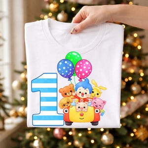 May include: A white t-shirt featuring a large blue and white striped number one next to a yellow car carrying a cartoon character, a bear, a dog, a pig, and a cat, with green, blue, and pink polka-dot balloons floating above the vehicle.