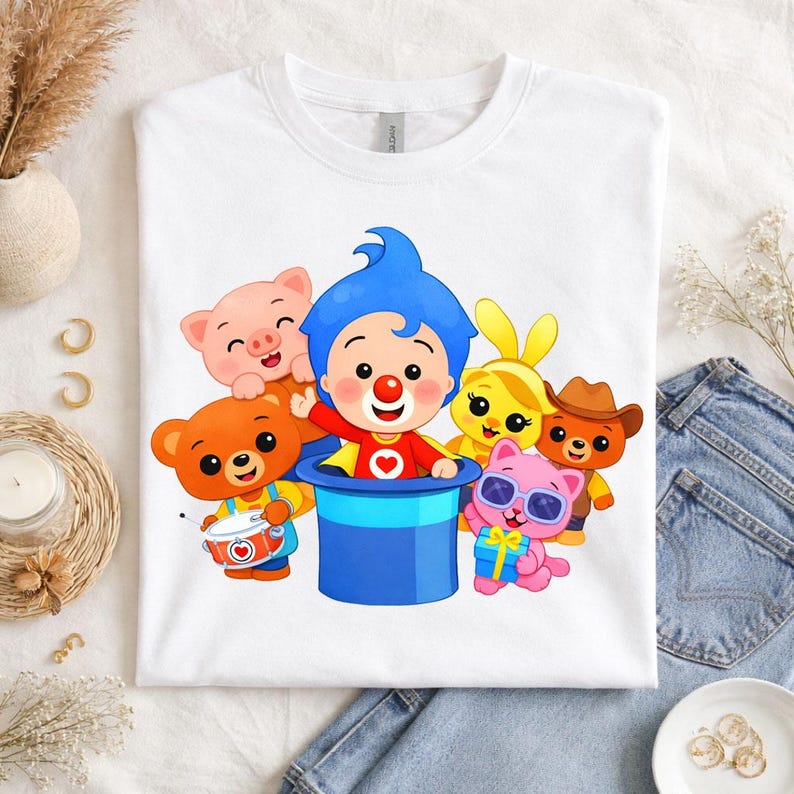 May include: A white t-shirt featuring a colorful graphic of a blue-haired character emerging from a blue top hat, surrounded by a pig, a bear playing a drum, a yellow rabbit, a pink cat with sunglasses holding a gift, and a bear in a cowboy hat.