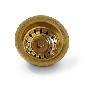 May include: A circular brass sink strainer featuring a polished metallic finish. The component includes a central knob for manual operation and a series of evenly spaced, teardrop-shaped drainage perforations arranged in a ring around the center.