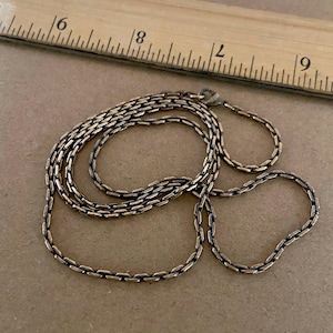 May include: A silver-toned metal chain necklace with a textured, interlocking link design. The necklace is positioned next to a wooden ruler, showing a length of approximately 18 inches from the clasp to the end of the chain.