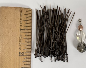 May include: A pile of 100 brown head pins, approximately 1 inch long, next to a ruler and a beaded charm.  The head pins are used for jewelry making.