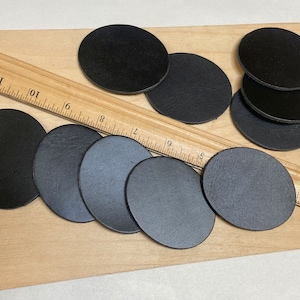 May include: Eight black leather circles of varying sizes on a wooden surface with a ruler.