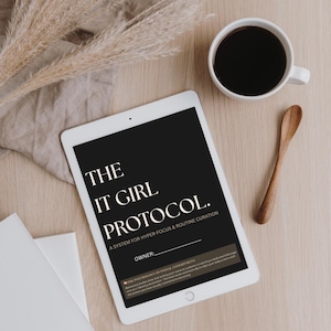 May include: A white tablet displaying a black screen with the white text THE IT GIRL PROTOCOL. A SYSTEM FOR HYPER-FOCUS & ROUTINE CURATION. OWNER: followed by a line and a paragraph titled THE PSYCHOLOGY OF INITIAL COMMITMENT in white font.