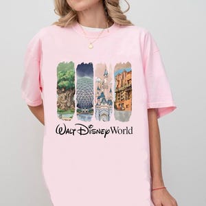 May include: Pale pink t-shirt with a graphic showcasing Walt Disney World attractions. The design includes the Tree of Life, Spaceship Earth, Cinderella Castle, and Hollywood Tower Hotel, with "Walt Disney World" written underneath.