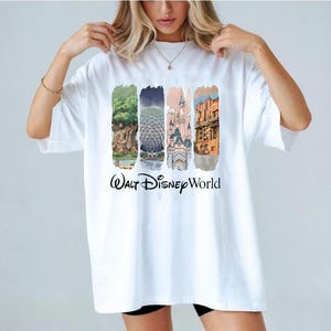 May include: White t-shirt with colourful illustrations of Walt Disney World landmarks. The shirt features images of a tree, Spaceship Earth, a castle, and a building, with the words "Walt Disney World" printed below the images.