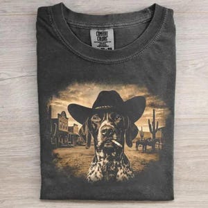 May include: Dark gray t-shirt featuring a dog wearing a cowboy hat and smoking a cigarette, set against a sepia-toned Western scene. The shirt has a Comfort Colors tag.