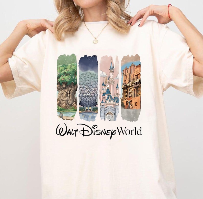May include: A cream-coloured t-shirt with a colourful graphic of Walt Disney World landmarks. The design includes images of the Tree of Life, Spaceship Earth, Cinderella Castle, and the Hollywood Tower Hotel, with "Walt Disney World" text.