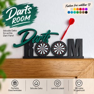 Könnte beinhalten: Ein schwarzes 3D-gedrucktes Schild mit dem Schriftzug Darts ROOM, bei dem die beiden O durch runde Dartscheiben ersetzt sind. Ein roter Dartpfeil steckt in der rechten Dartscheibe. Über dem Wort Darts steht der Schriftzug in Dunkelgrün.
