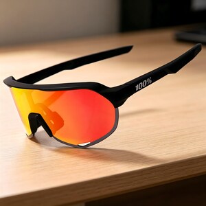 May include: Black sports sunglasses with a vibrant red and yellow gradient lens. The frame is black, with the text "100%" printed on the temple. The sunglasses are designed for sports and outdoor activities.