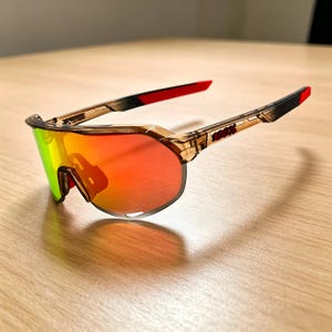 May include: Sport sunglasses with a brown frame and red and black accents. The lenses have a gradient of colors, including red, orange, and green. The brand name "100%" is printed on the arm.