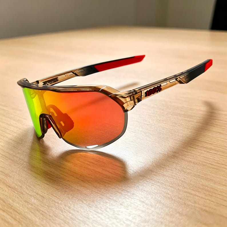 May include: Sport sunglasses with a brown frame and red and black accents. The lenses have a gradient of colors, including red, orange, and green. The brand name "100%" is printed on the arm.