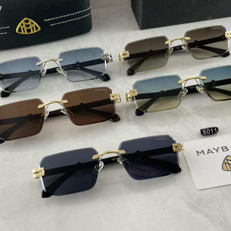 May include: An assortment of rimless sunglasses with gold-tone accents and tinted lenses. The lenses vary in color, including blue, brown, and black. The brand name "MAYBACH" is visible on some of the frames. A black case with a gold emblem is also present.