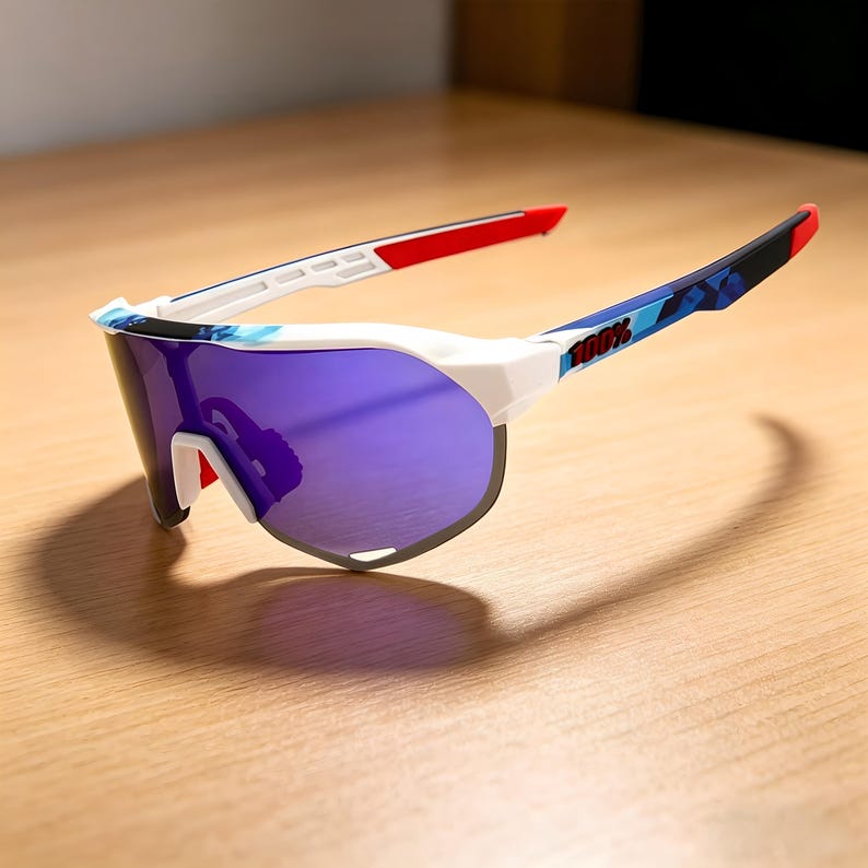 May include: White and blue sports sunglasses with purple lenses. The frames have red accents on the temples and a blue camouflage pattern on the arms. The text "100%" is printed on the arm.