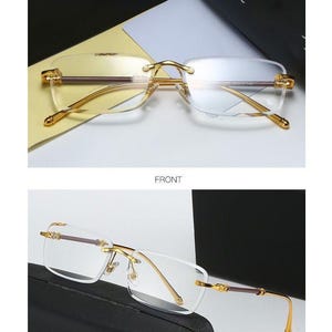 May include: Rimless eyeglasses with gold-colored metal frames and temples. The lenses are clear, and the top bar is a dark brown color. The text "GOLD TEA/TRANSPARENT" is at the top of the image. The image also shows the text "FRONT" and "45 DISPLAY".