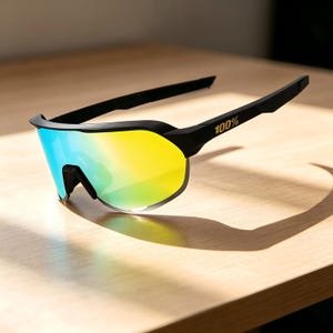May include: Black sports sunglasses with a gradient lens that transitions from blue to yellow. The frame is black, and the right temple arm features the text "100%". The sunglasses are designed for sports and outdoor activities.