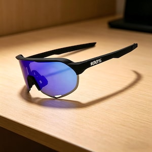 May include: Black sports sunglasses with blue mirrored lenses. The sunglasses have a sleek, modern design with the text "100%" printed on the arm. The lenses are a vibrant blue color, and the frame is black.