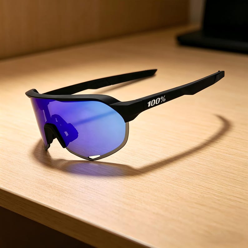 May include: Black sports sunglasses with blue mirrored lenses. The sunglasses have a sleek, modern design with the text "100%" printed on the arm. The lenses are a vibrant blue color, and the frame is black.