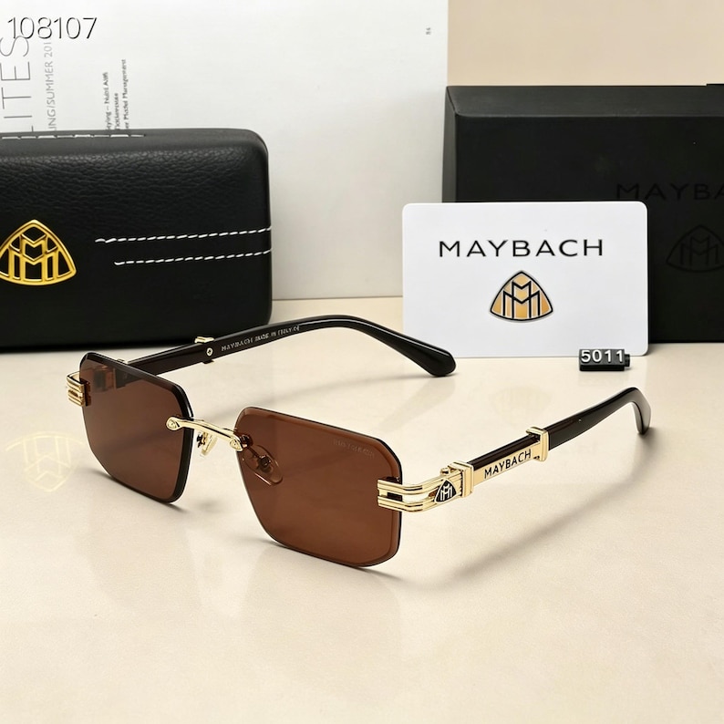 May include: Brown rectangular sunglasses with gold accents and the brand name "MAYBACH" visible on the temples. The sunglasses are displayed with a black case and a white card with the brand logo.