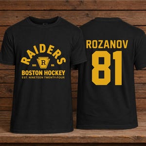 May include: Black t-shirt with gold lettering and numbers. The front reads "RAIDERS" above "BOSTON HOCKEY" and "EST. NINETEEN TWENTY-FOUR". The back displays "ROZANOV" and the number "81".