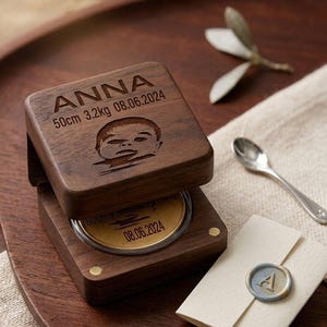 Könnte beinhalten: Personalisierte Holz-Andenkenbox mit dem Namen "ANNA", Geburtsdaten des Babys: 50cm, 3,2kg und 08.06.2024, sowie einer Babygesicht-Illustration. Enthält eine goldfarbene Münze. Ein Umschlag mit Wachssiegel ist ebenfalls vorhanden.