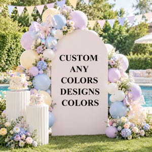 Op de afbeelding: Een groot boogvormig bord met de tekst CUSTOM ANY COLORS DESIGNS COLORS, omringd door een ballonslinger in pastelblauw, geel en paars, met iriserende strikken, bloemstukken en twee witte gecanneleerde sokkels met taarten.