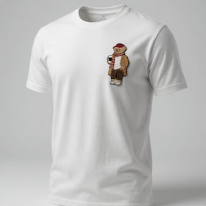 May include: White t-shirt with a small embroidered patch of a bear wearing a red hat, scarf, and coat, holding a coffee cup. The bear is in a standing pose. The shirt has a crew neck and short sleeves.