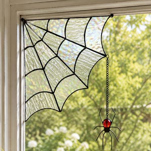 May include: A stained glass spider web corner piece with iridescent clear glass panels and black metal framing. A small black metal spider with a single round red glass bead for a body hangs from the web by a thin black metal chain.