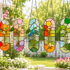 May include: Five hanging stained glass planters with colorful designs and black metal chains. Each planter holds a small plant in a glass vase. The glass features vibrant colors like orange, pink, blue, and green, depicting landscapes and suns.