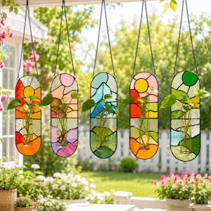 May include: Five hanging stained glass planters with black chain hangers. Each planter features a unique landscape design with vibrant colors, including orange, pink, blue, yellow, and green. Each planter holds a small plant in a glass vase.