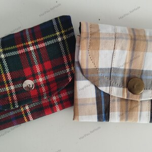 Op de afbeelding: Twee kleine, handgemaakte stoffen zakjes. Eén is een donker plaid met rood, groen en marineblauw. De andere is een licht plaid met beige, wit en blauw. Beide hebben een klepsluiting met een knoop.