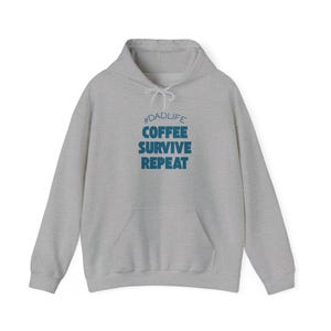 May include: A light grey hoodie with a front pocket and a drawstring hood. The text "#DADLIFE COFFEE SURVIVE REPEAT" is printed in blue on the front. The hoodie is made of a soft, comfortable material.