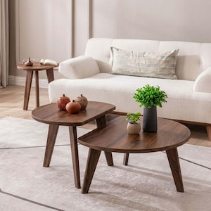 May include: A set of three dark brown wooden tables with semi-circular tops and angled legs. The tables are arranged in a tiered formation, with two tables nested together in the foreground and one smaller table positioned separately to the left.