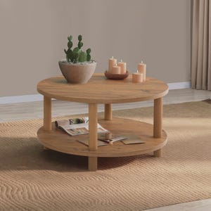 May include: A round, two-tiered wooden coffee table with a light brown wood grain finish. The top surface holds a potted green cactus in a gray bowl and three cylindrical beige candles in a small brown dish. An open magazine rests on the lower shelf.