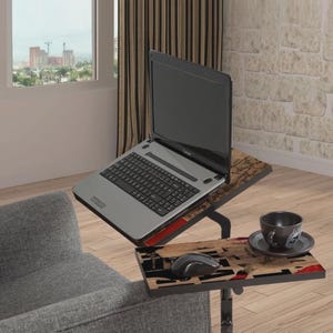 Puede incluir: Un portátil plateado sobre una mesa para portátil ajustable de dos niveles. La parte superior sostiene el portátil, la inferior tiene un ratón y una taza de café. La mesa tiene un marco negro y un diseño de vetas de madera.