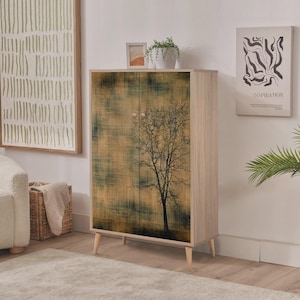 Puede incluir: Un mueble de madera con un diseño de árbol en las puertas. El mueble tiene un marco y patas de madera clara. Las puertas presentan un fondo texturizado con un árbol silueteado. Cada puerta tiene un pequeño pomo redondo rosa.
