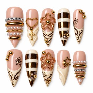 May include: A set of ten press-on nails featuring a nude base with various embellishments including gold rings, white pearls, clear rhinestones, metallic stripes, floral accents, a cross charm, star shapes, and intricate brown swirl patterns.